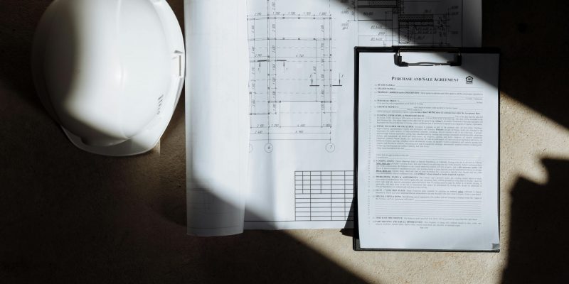 Top view of construction documents and hard hat in sunlight, capturing planning essence.